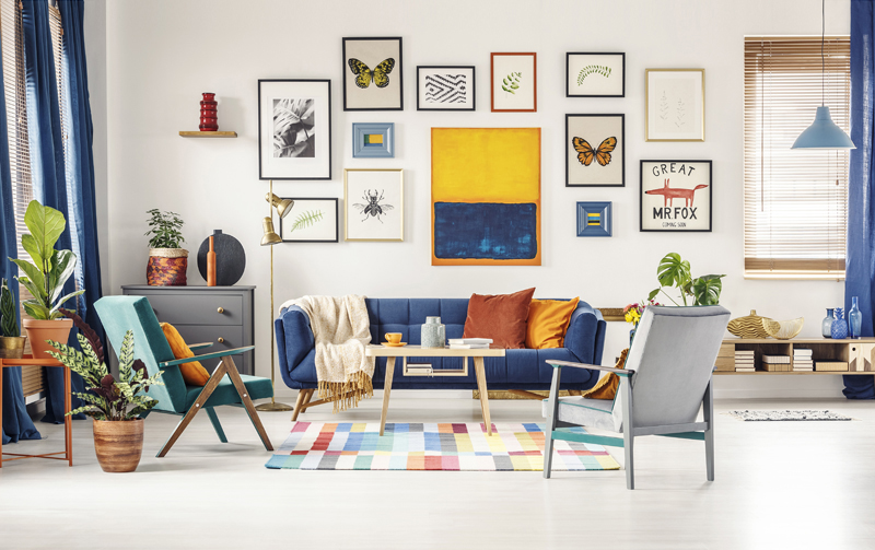 Simple posters gallery hanging on the wall in bright living room interior with blue sofa, two armchairs, fresh plants and wooden coffee table standing on colorful carpet