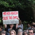 Woman holds sign that reads Never Again, Close The Camps